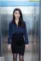 A woman in a blue shirt and black skirt standing in an elevator.