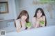 Two young women sitting on a white couch eating watermelon.