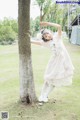 A young girl in a white dress leaning against a tree.