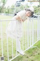 A little girl in a white dress leaning on a fence.