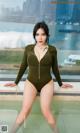 A woman in a green bodysuit posing by a pool.